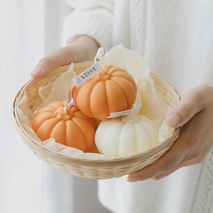 Two orange and white scented pumpkin candles held in a basket, showcasing cozy pumpkin-shaped designs and warm fragrances, perfect for adding a seasonal touch to your fall decor.