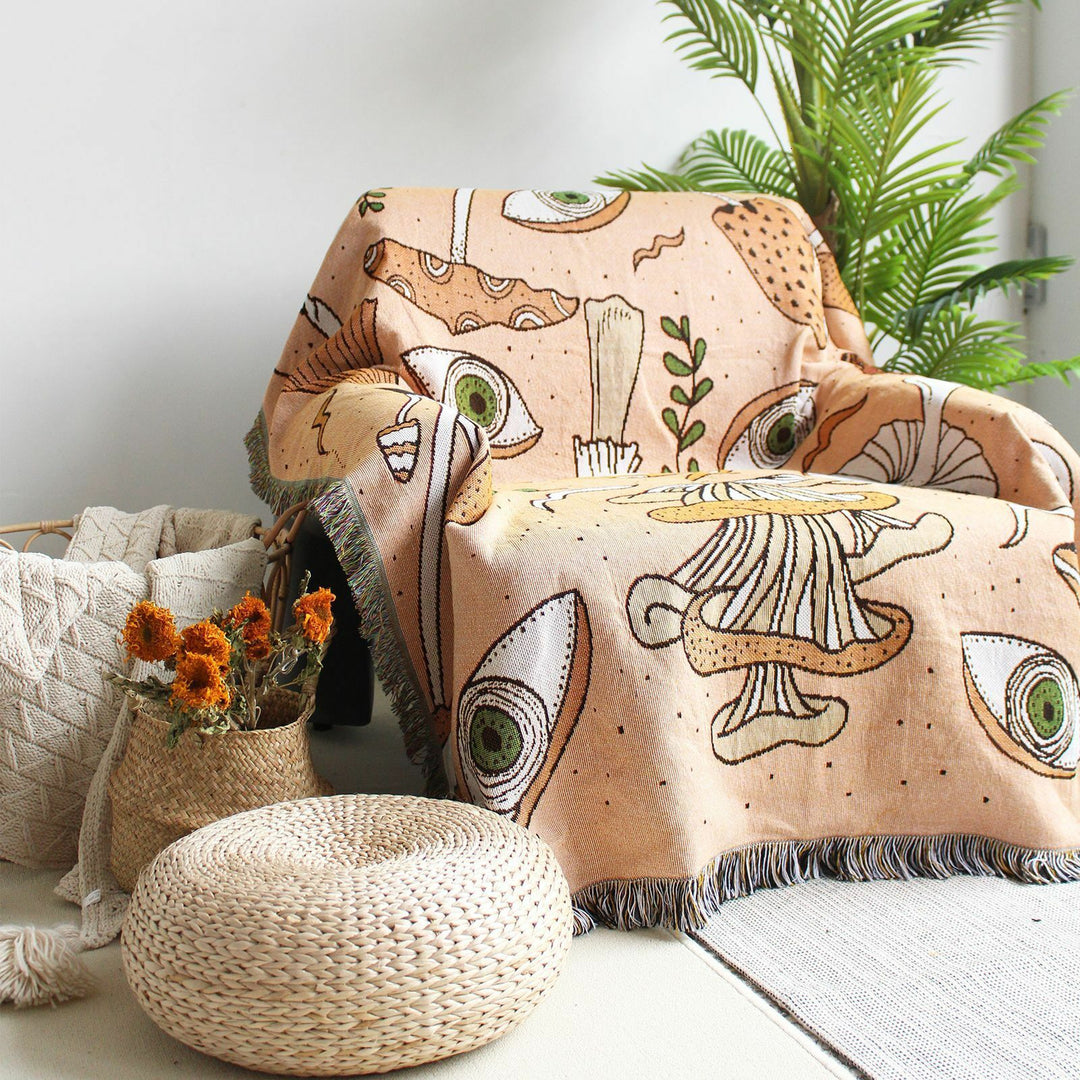 VibeCore Shroom Magic Woven Blanket draped over a chair in a living room, showcasing its whimsical mushroom pattern and soft, reversible cotton texture for a cozy, aesthetic touch.