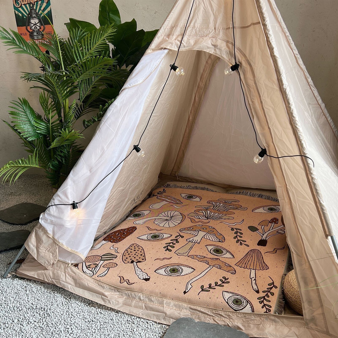 VibeCore Shroom Magic Woven Blanket used as a floor cover in a tent, featuring its dreamy mushroom design and soft, reversible cotton texture, creating a cozy atmosphere.