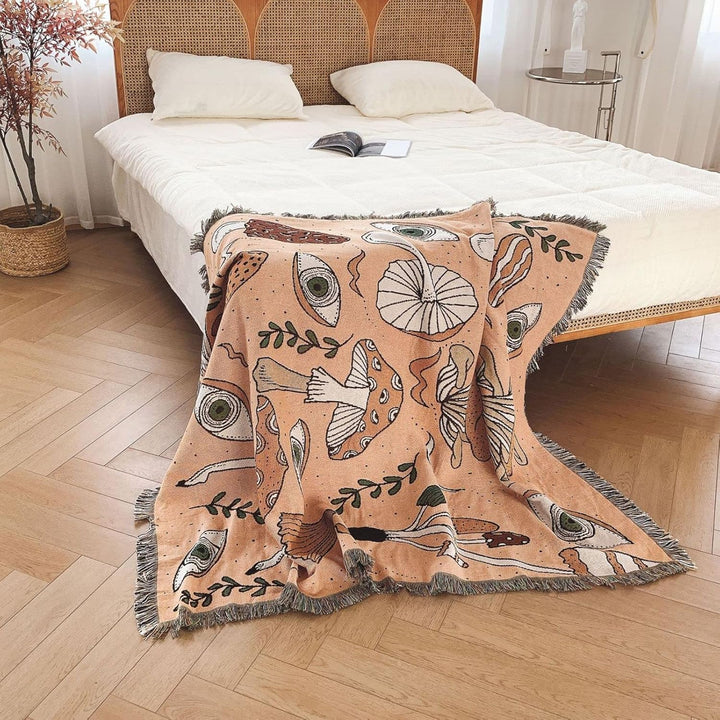 VibeCore Shroom Magic Woven Blanket draped over the corner of a bed, showcasing its dreamy mushroom pattern and soft woven texture in a cozy, ambient setting.