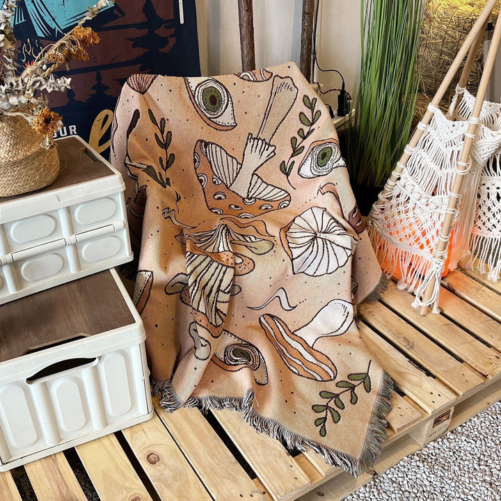 VibeCore Shroom Magic Woven Blanket draped over a wooden chair, highlighting its soft texture and reversible mushroom-themed design in a cozy, aesthetic setting.