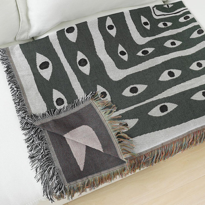 VibeCore Snake-Eye Woven Blanket, folded neatly, featuring its bold snake-eye design. Made from 100% combed cotton, this blanket offers a stylish, versatile accent for any room, combining comfort with an edgy, mysterious aesthetic.