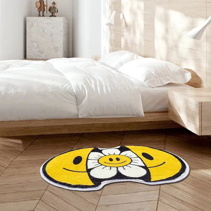 VibeCore Sunshine Split Smiley Accent Rug beside a bed, featuring a playful design with a smiling face splitting open to reveal a vibrant sunflower, adding charm and color to the room.
