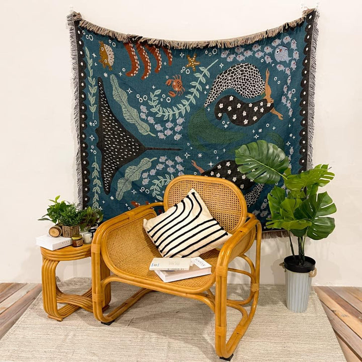VibeCore Swimming Mermaids Woven Blanket as a wall hanging, showcasing an enchanting mermaid design and soft 100% combed cotton texture.