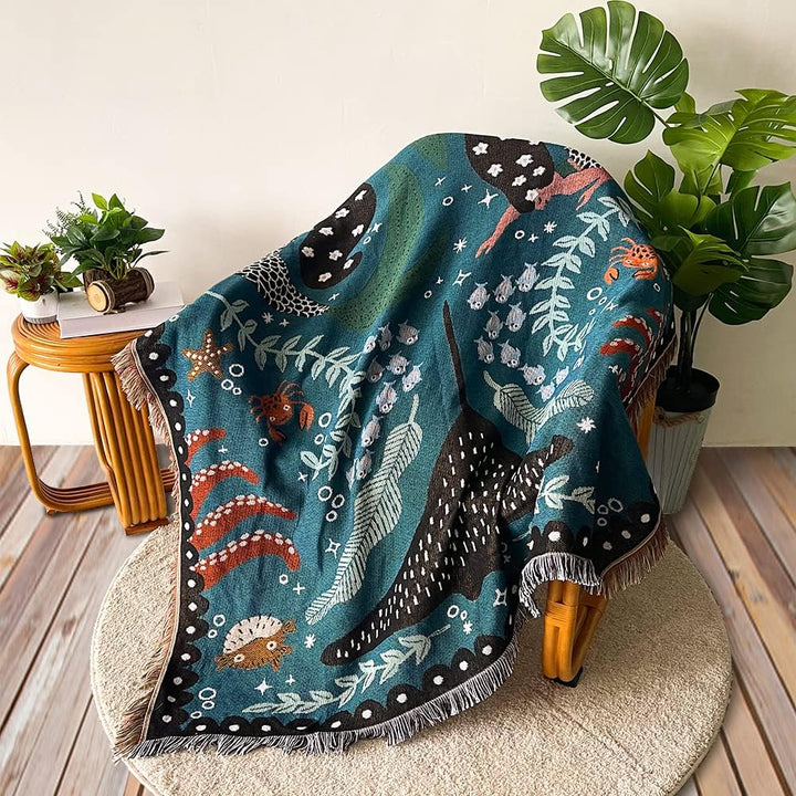 VibeCore Swimming Mermaids Woven Blanket on chair, featuring an enchanting mermaid design and soft 100% combed cotton fabric.