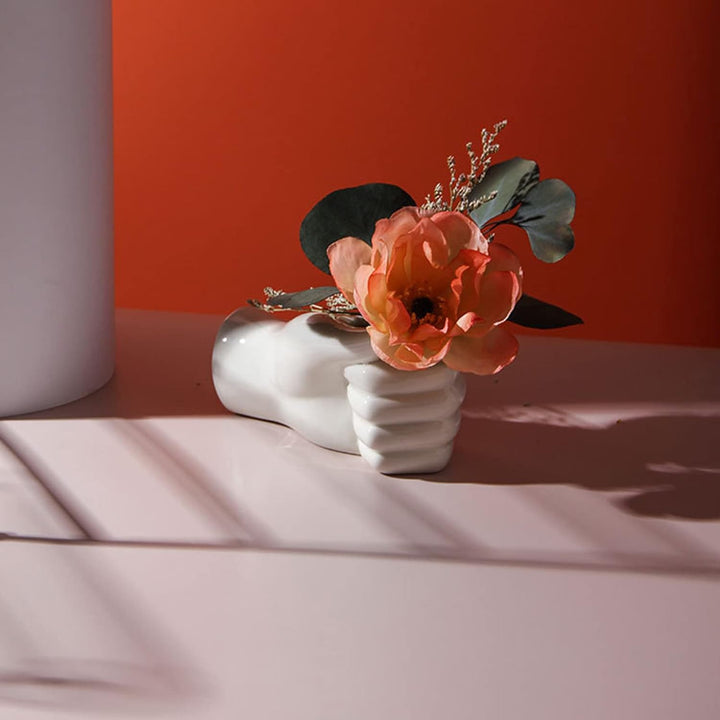 Unique hand-shaped ceramic vase with flower, displayed on shelf for a bold modern touch.