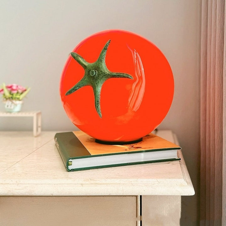 A bold, red glass tomato-shaped table lamp glowing warmly, adding a cozy and eclectic touch to any space. Perfect for funky and dopamine decor aesthetics.