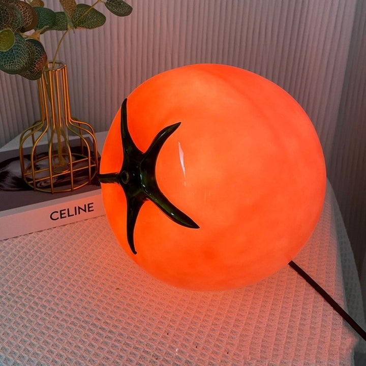 A glowing red glass tomato-shaped table lamp, casting a warm and cozy light. Its playful yet sophisticated design makes it a standout piece for eclectic and dopamine decor aesthetics.