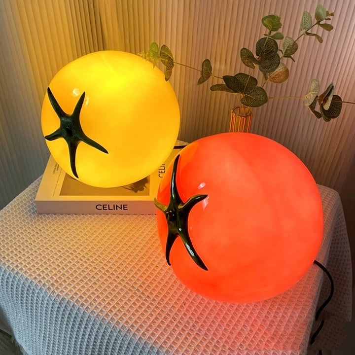 A glowing, tomato-inspired glass table lamp in vibrant yellow and red, casting a warm, cozy light and adding a playful, eclectic charm to any space.