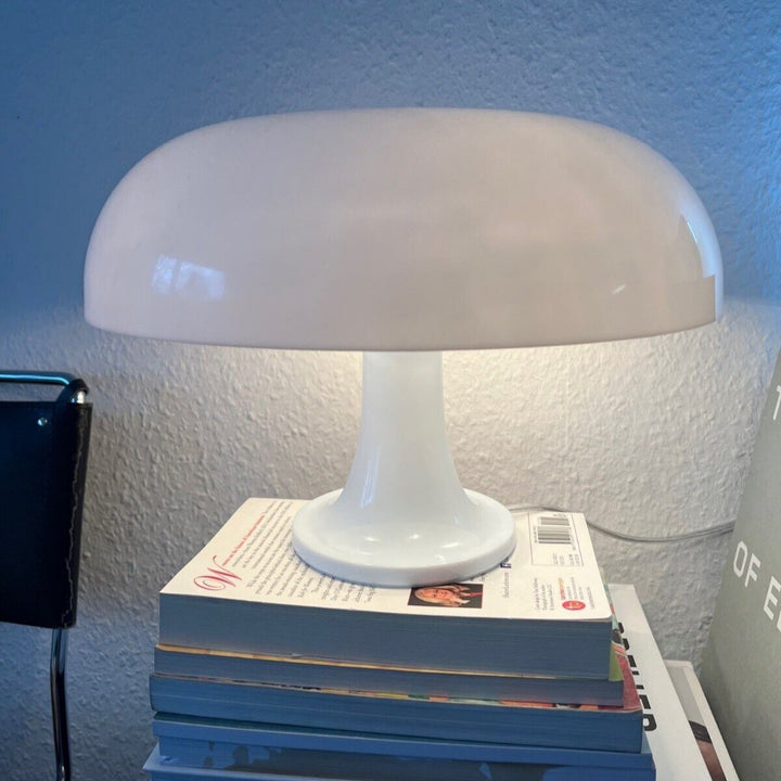 VibeCore Vintage 60s Mushroom Lamp in white, lit up, resting on a stack of books, creating a cozy and stylish ambiance.