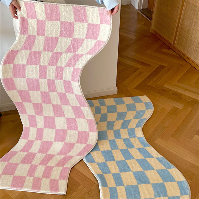 Aesthetic pink "Wavy Checkerboard Accent Rug" being held up beside a blue "Wavy Checkerboard Accent Rug" on the floor. The dynamic checkerboard pattern with a wavy twist is highlighted in both colors, showcasing the soft, plush texture and non-slip backing of each rug. Perfect for adding style and comfort to any room.