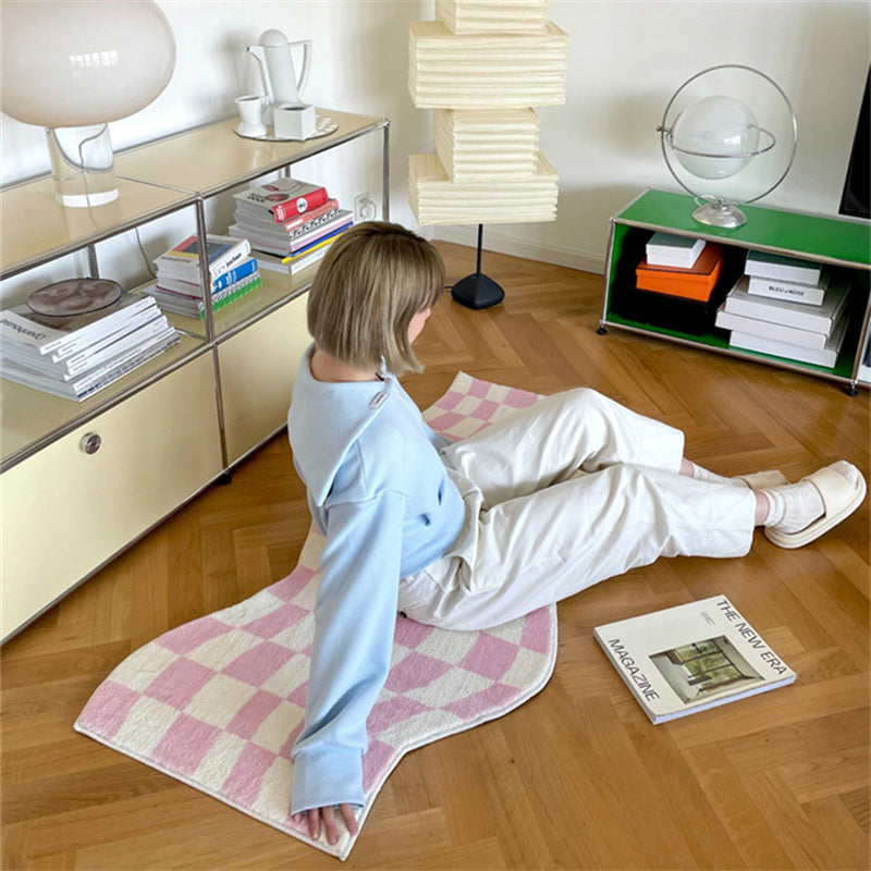 Aesthetic pink "Wavy Checkerboard Accent Rug" displayed on a wooden floor with a girl sitting on it. The dynamic checkerboard pattern with a wavy twist adds a stylish touch, while the soft, plush texture and non-slip backing provide comfort and stability in any room.