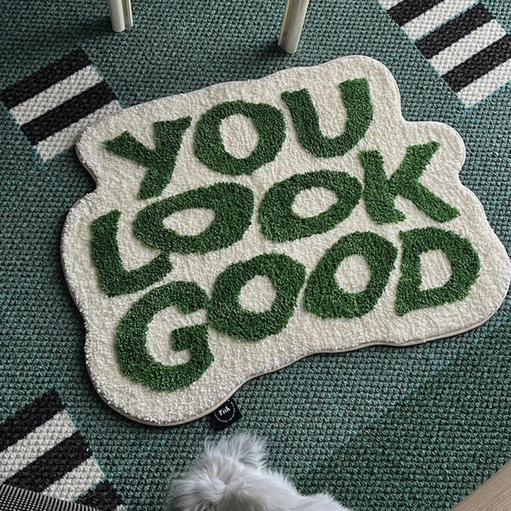 Aerial view of the VibeCore You Look Good Accent Rug in green, highlighting its vibrant quote design, soft plush texture, non-slip backing, and cute rug appeal. This modern, playful rug adds personality and comfort to bedrooms, dorms, or living rooms. Its contemporary aesthetic complements any space, bringing a cozy and motivational touch. Ideal for those looking to brighten their home with a fun, uplifting rug that adds a cheerful vibe to any room.