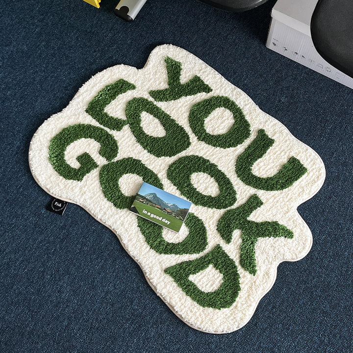 VibeCore You Look Good Accent Rug in green, with a card placed on it for size comparison. The rug features an uplifting quote design, soft plush texture, and non-slip backing. This cute rug adds a playful and modern touch to bedrooms, dorms, or living rooms, making it an ideal choice for contemporary spaces. Its vibrant design brings personality and comfort, creating a cozy, motivational accent in any room. Perfect for those seeking a fun and aesthetic rug to complement their decor.