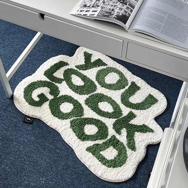 VibeCore You Look Good Accent Rug in green, placed under a desk, showcasing its uplifting quote design, soft plush texture, and non-slip backing. This cute rug adds a playful, modern touch to any space, perfect for brightening up bedrooms, dorms, or living rooms. Its vibrant design brings personality and comfort to your room, making it an ideal choice for contemporary decor. A cozy, motivational accent rug that complements your workspace or any part of your home.