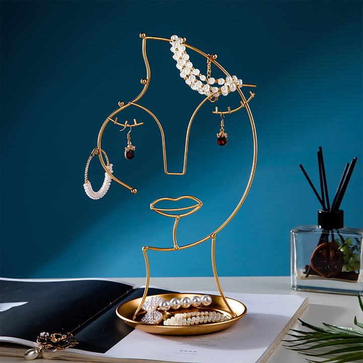 VibeCore Abstract Beauty Jewelry Stand with jewelry on it, featuring an abstract female face design in gold iron metal, keeping earrings, necklaces, and rings neatly organized.