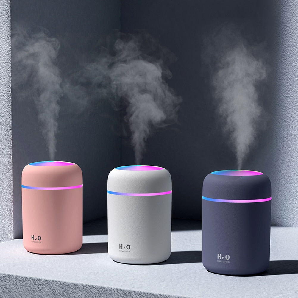 All three diffusers (white, gray, and blossom) emitting mist with vibrant LED lights, placed elegantly on a table, creating a calming ambiance in the room.