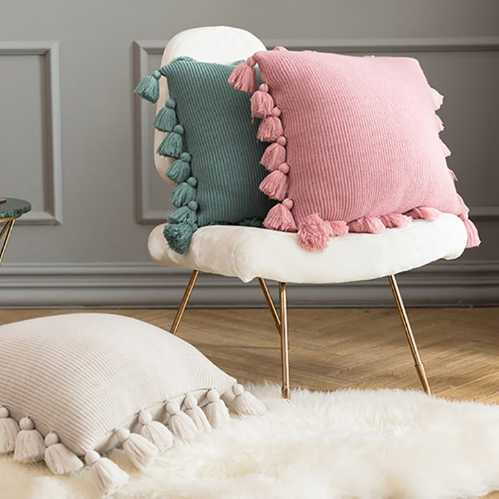 VibeCore Nordic Style Hand-Knitted Pillow Covers in Blossom, Dark Gray, and Ivory stacked on a sofa in a cozy living room, adding a boho touch with fringe details.