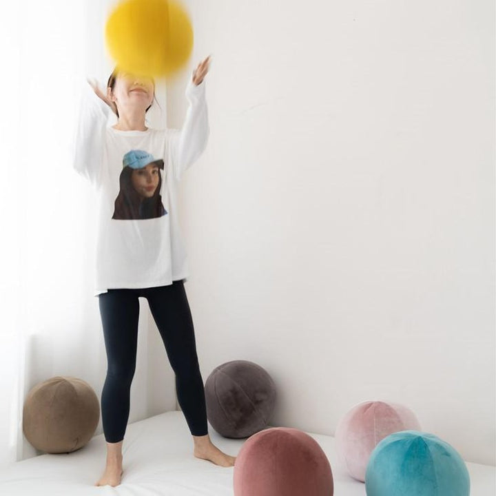 VibeCore Velvet Ball Pillow in mauve, girl playfully tossing plush round velvet pillow in the air, adding modern and playful decor to any room.